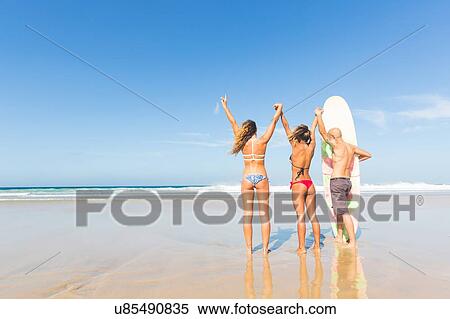 Stock Photography - Man and two young women wearing swimwear holding hands on beach, El Cotillo, Fuerteventura, Spain. Fotosearch