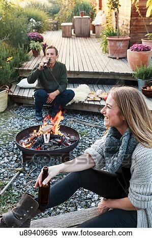 Man and woman sitting by fire pit with beer, relaxing View Large Photo Image Stock Photography - Man and woman sitting by fire pit with beer, relaxing. Fotosearch