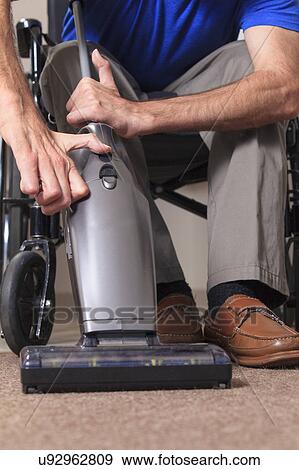 Stock Photo - Man in wheelchair vacuuming his house. Fotosearch