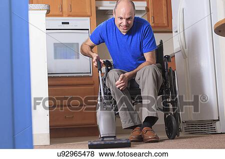 Stock Photo - Man in wheelchair vacuuming his house. Fotosearch