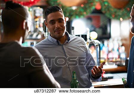 Stock Photo - Man leaning against counter in public house talking to friend. Fotosearch