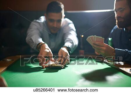 Stock Image - Man picking up card game winnings at pub card table. Fotosearch