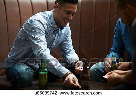 Stock Image - Man placing coin on table whilst playing cards in traditional UK pub. Fotosearch