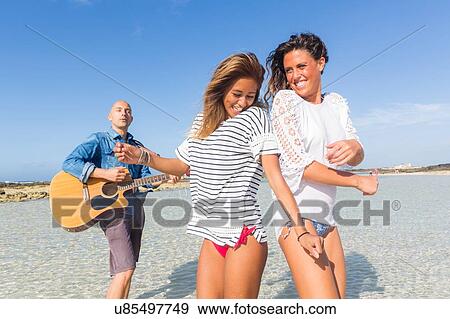 Man playing acoustic guitar and two happy young women dancing on beach, El Cotillo, Fuerteventura, Spain View Large Photo Image Stock Photo - Man playing acoustic guitar and two happy young women dancing on beach, El Cotillo, Fuerteventura, Spain. Fotosearch