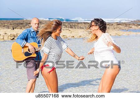 Man playing acoustic guitar and two young women dancing on beach, El Cotillo, Fuerteventura, Spain View Large Photo Image Stock Photo - Man playing acoustic guitar and two young women dancing on beach, El Cotillo, Fuerteventura, Spain. Fotosearch