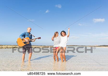 Man playing acoustic guitar with two young women dancing on beach, El Cotillo, Fuerteventura, Spain View Large Photo Image Stock Photography - Man playing acoustic guitar with two young women dancing on beach, El Cotillo, Fuerteventura, Spain. Fotosearch