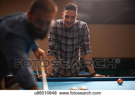 Stock Photo - Man playing pool, friend in background. Fotosearch