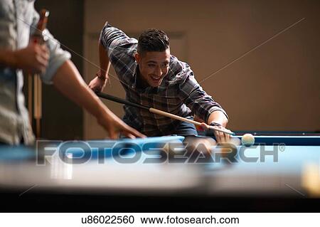 Stock Image - Man playing pool, friend with beer in foreground. Fotosearch