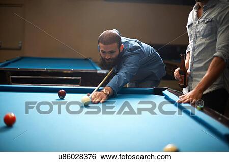 Stock Photograph - Man playing pool, friend with beer in foreground. Fotosearch