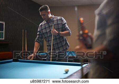 Stock Image - Man preparing to play pool, friend with beer in foreground. Fotosearch