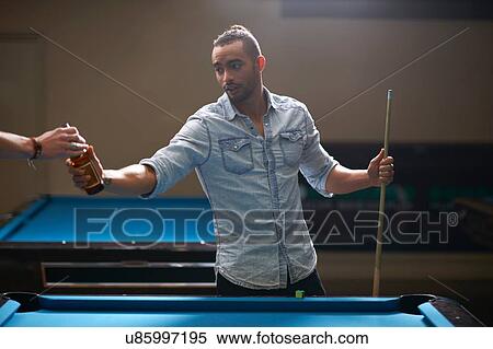 Stock Photography - Man taking beer from friend at pool table. Fotosearch
