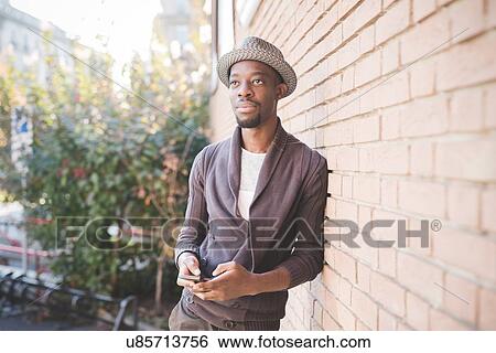 Stock Photograph - Man with smartphone leaning against brick wall. Fotosearch