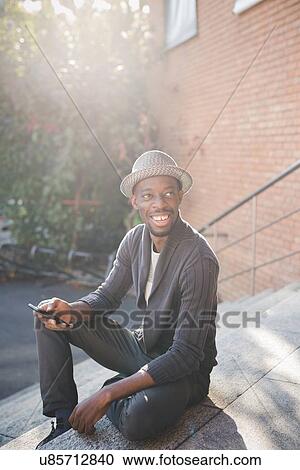 Stock Image - Man with smartphone sitting on steps. Fotosearch