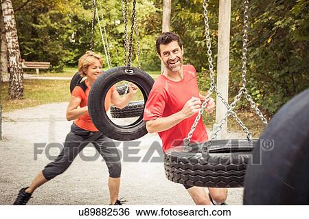 Stock Photograph - Mature couple running around tyre swings smiling. Fotosearch