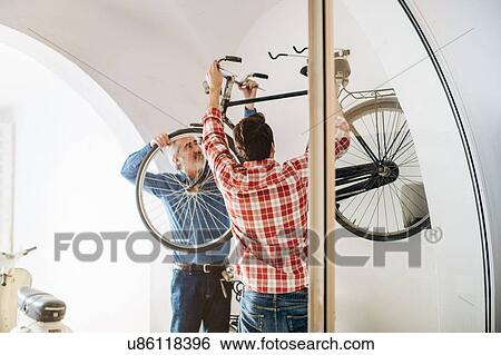 Mature man and adult son removing bicycle from rack in garage View Large Photo Image Stock Photograph - Mature man and adult son removing bicycle from rack in garage. Fotosearch