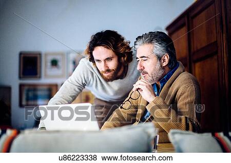 Mature man and adult son sitting in living room browsing laptop View Large Photo Image Stock Photo - Mature man and adult son sitting in living room browsing laptop. Fotosearch