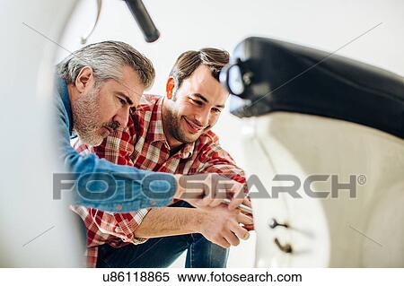 Stock Photography - Mature man and adult son to repairing moped in garage. Fotosearch