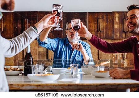 Stock Photo - Mature man and adult sons raising a glass of red wine at dining table. Fotosearch