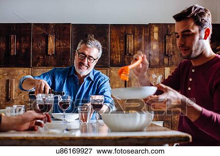 Mature man and adult sons serving Italian lunch at dining table View Large Photo Image Stock Photo - Mature man and adult sons serving Italian lunch at dining table. Fotosearch