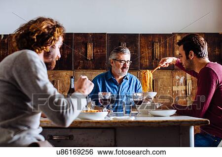 Mature man and adult sons serving spaghetti lunch at dining table View Large Photo Image Stock Photograph - Mature man and adult sons serving spaghetti lunch at dining table. Fotosearch