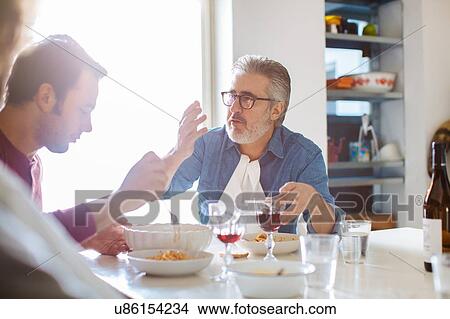 Mature man and adult sons talking at dining table View Large Photo Image Picture - Mature man and adult sons talking at dining table. Fotosearch
