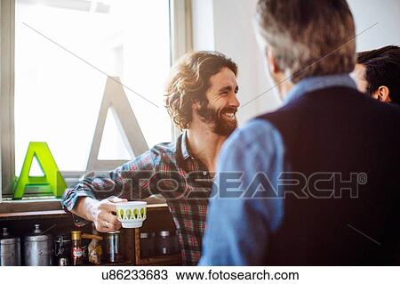 Stock Image - Mature man and two adult sons chatting and drinking coffee in living room. Fotosearch