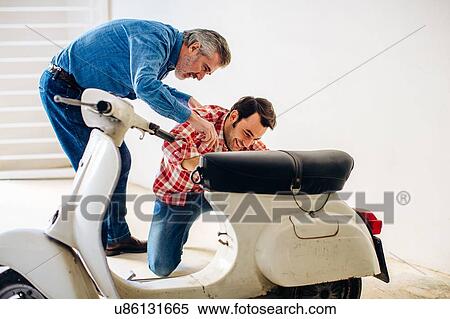 Stock Photography - Mature man helping adult son to repair moped in garage. Fotosearch