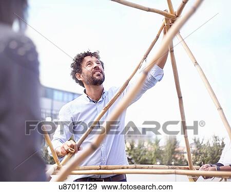 Mature man in team building task building wooden structure smiling View Large Photo Image Stock Photo - Mature man in team building task building wooden structure smiling. Fotosearch
