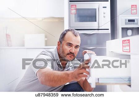 Stock Photo - Mature man inspecting drawers in kitchen showroom. Fotosearch
