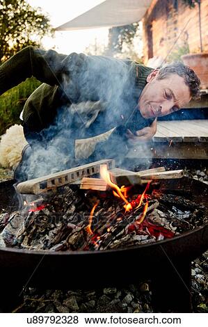 Stock Photo - Mature man leaning to inspect fire pit. Fotosearch
