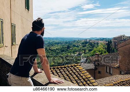 Stock Image - Mature man looking out over rooftops and distant view, San Miniato, Tuscany, Italy. Fotosearch