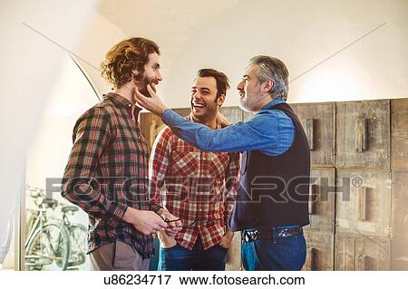 Stock Photo - Mature man teasing adult sons beard in living room. Fotosearch