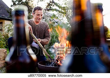 Mature man using stick to poke fire pit View Large Photo Image Stock Photography - Mature man using stick to poke fire pit. Fotosearch