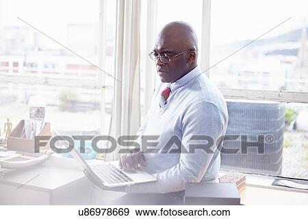 Mature man wearing eye glasses in office using laptop View Large Photo Image Stock Photo - Mature man wearing eye glasses in office using laptop. Fotosearch