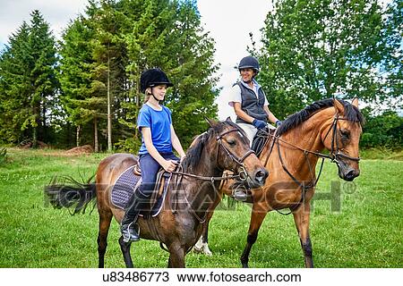 Mature woman and girl on horseback wearing riding hats smiling View Large Photo Image Stock Image - Mature woman and girl on horseback wearing riding hats smiling. Fotosearch