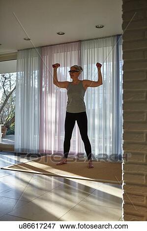 Stock Photo - Mature woman exercising with dumbbells in front of patio doors. Fotosearch