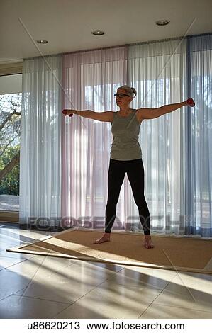 Stock Image - Mature woman weight lifting dumbbells in front of patio doors. Fotosearch