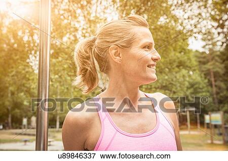 Stock Photo - Mature woman with ponytail in park wearing vest looking away smiling. Fotosearch