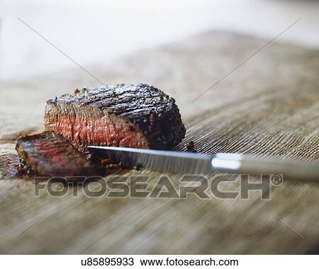 Stock Image - Medium rare steak with peppercorns, sliced with knife. Fotosearch