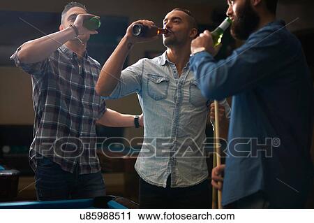 Stock Image - Men drinking beer at pool club. Fotosearch