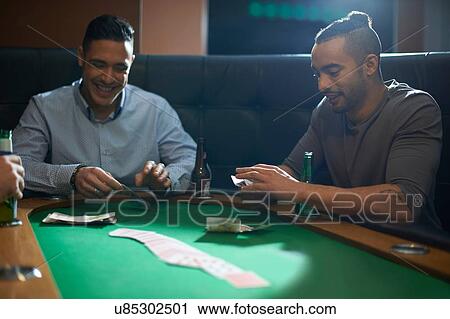 Stock Image - Men placing cash for card game at pub card table. Fotosearch