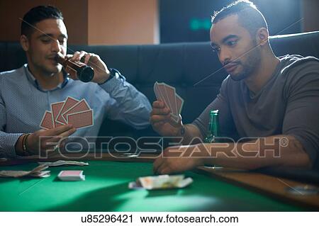 Stock Image - Men playing card game for cash at pub card table. Fotosearch