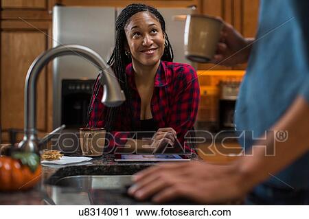 Stock Image - Mid adult couple at kitchen counter with digital tablet. Fotosearch