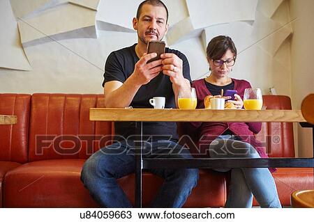 Mid adult couple reading smartphone texts in restaurant View Large Photo Image Stock Image - Mid adult couple reading smartphone texts in restaurant. Fotosearch