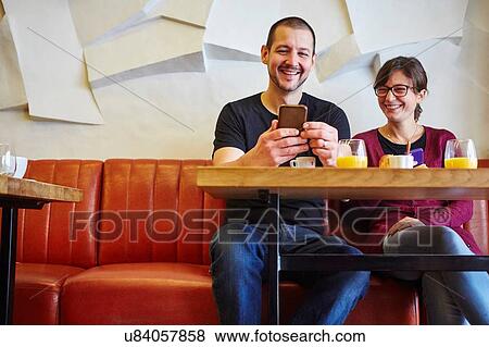 Mid adult couple reading smartphone text in restaurant View Large Photo Image Stock Photo - Mid adult couple reading smartphone text in restaurant. Fotosearch