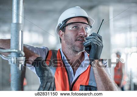 Stock Image - Mid adult male site manager using walkie talkie on construction site. Fotosearch