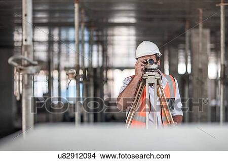 Mid adult male surveyor looking through theodolite on construction site View Large Photo Image Picture - Mid adult male surveyor looking through theodolite on construction site. Fotosearch