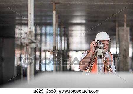 Stock Photo - Mid adult male surveyor using theodolite on construction site. Fotosearch