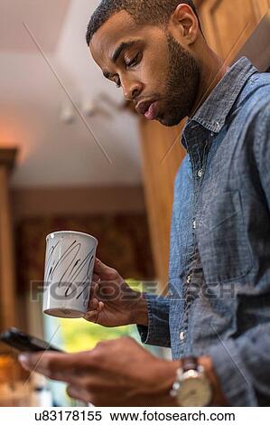 Mid adult man in kitchen reading smartphone text View Large Photo Image Stock Photography - Mid adult man in kitchen reading smartphone text. Fotosearch