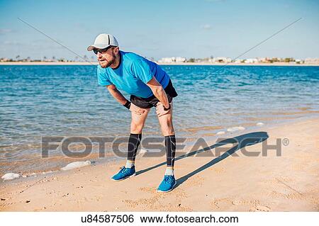 Stock Photograph - "Mid adult man on coastline bending forwards looking away, Dubai, United Arab Emirates". Fotosearch